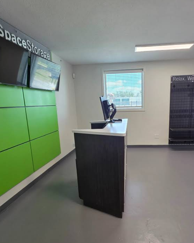 A reception desk in a brightly lit office with green wall panels and a black display rack, facing a window.