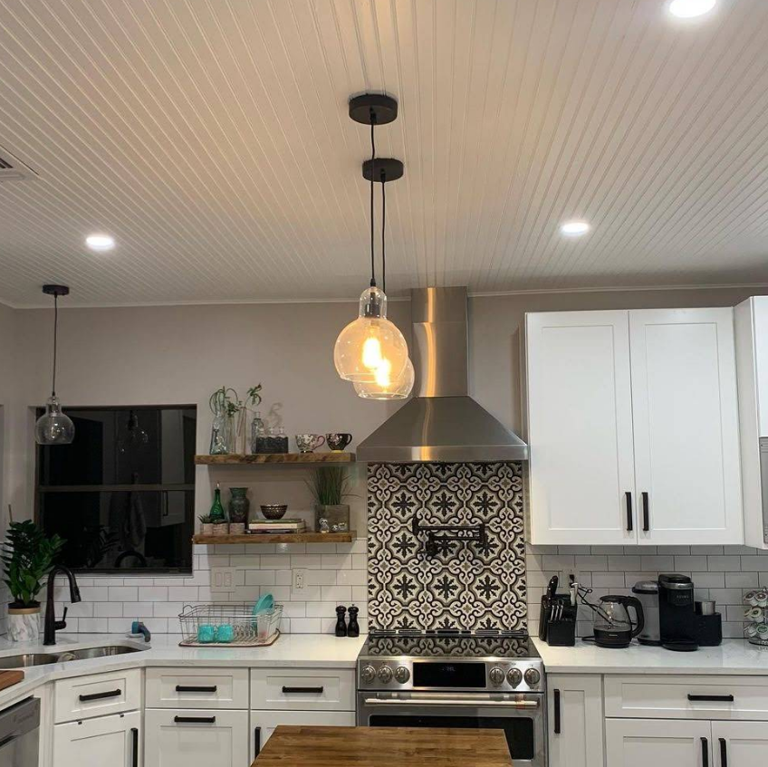 A kitchen features white cabinetry, white subway tiles, a black-and-white patterned backsplash, and two hanging pendant lights.