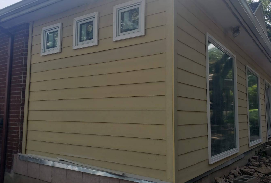 Exterior view of a yellow-sided house addition featuring three small square windows and a large rectangular window.