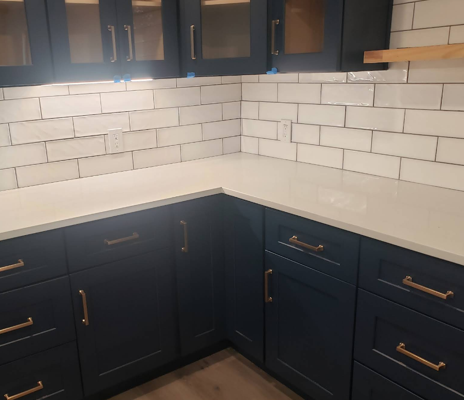 A corner kitchen view with dark blue cabinets, gold hardware, white quartz countertops, and a white subway tile backsplash.