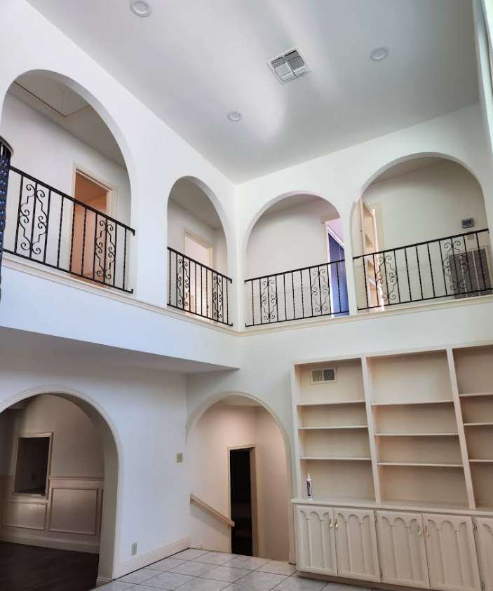 An interior view of a two-story foyer featuring white walls, arched openings, black wrought-iron railings, and built-in shelves.