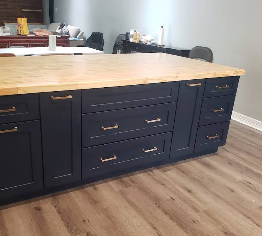 A kitchen island with matte dark blue cabinets and gold hardware, topped with a light wood butcher block countertop.