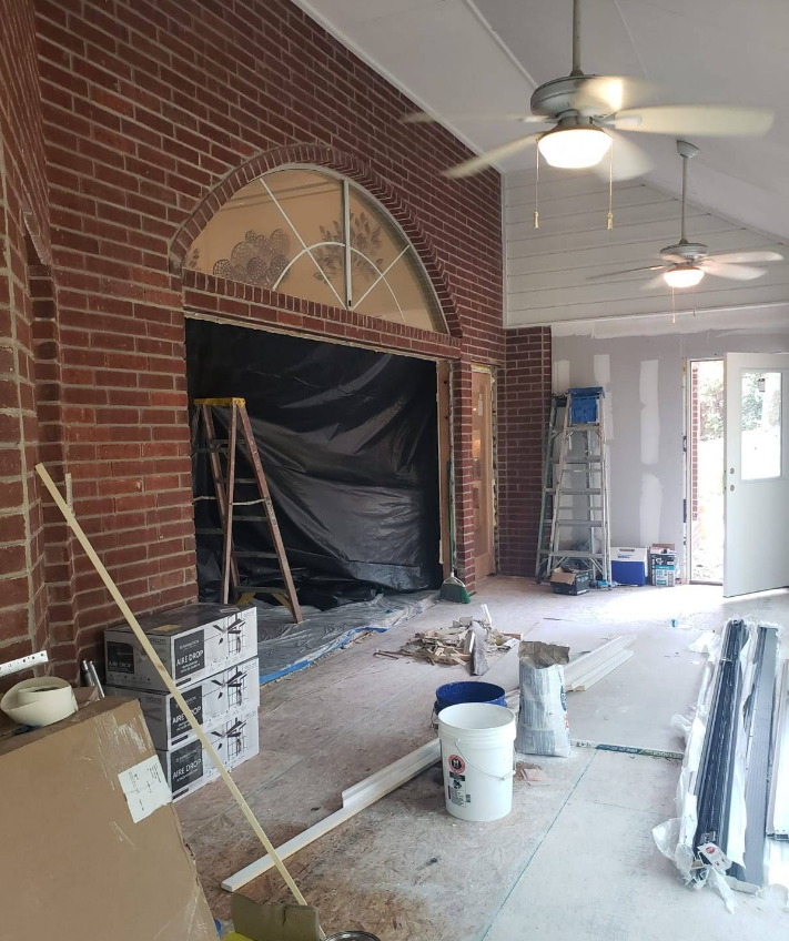 A construction project in progress featuring a brick wall, an arched window frame, ladders, and painting supplies.