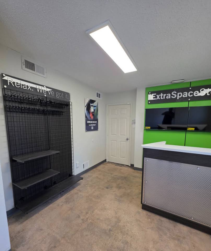An Extra Space Storage office featuring a white reception desk, a black grid display wall, and a door in a bright room.