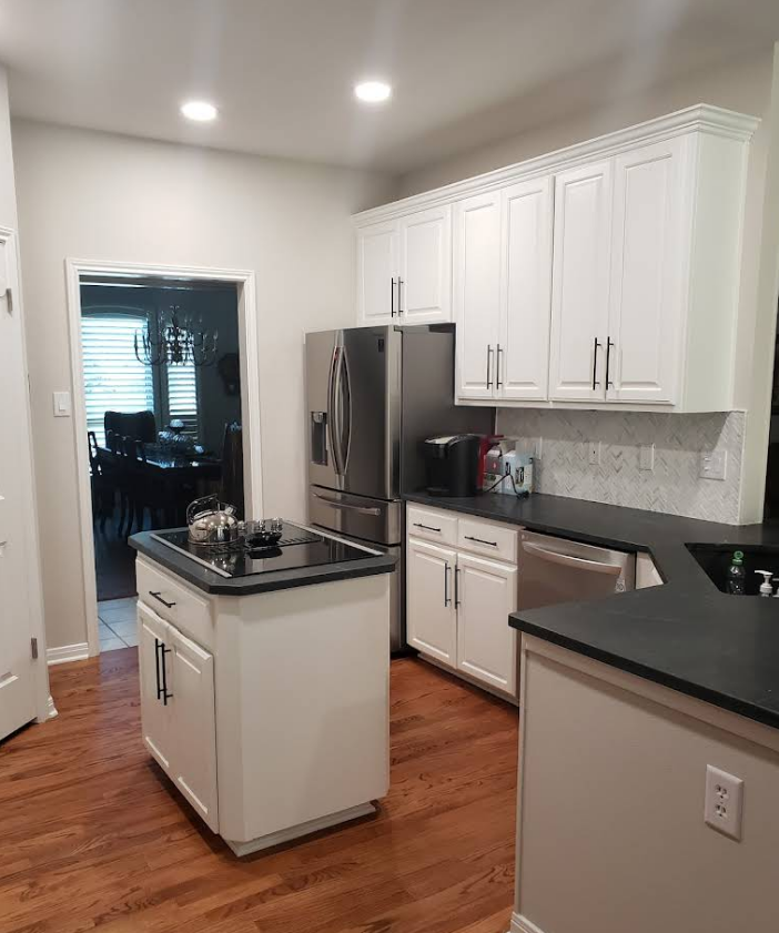 A kitchen featuring white cabinets, black countertops, a central island with a cooktop, and a stainless steel refrigerator.