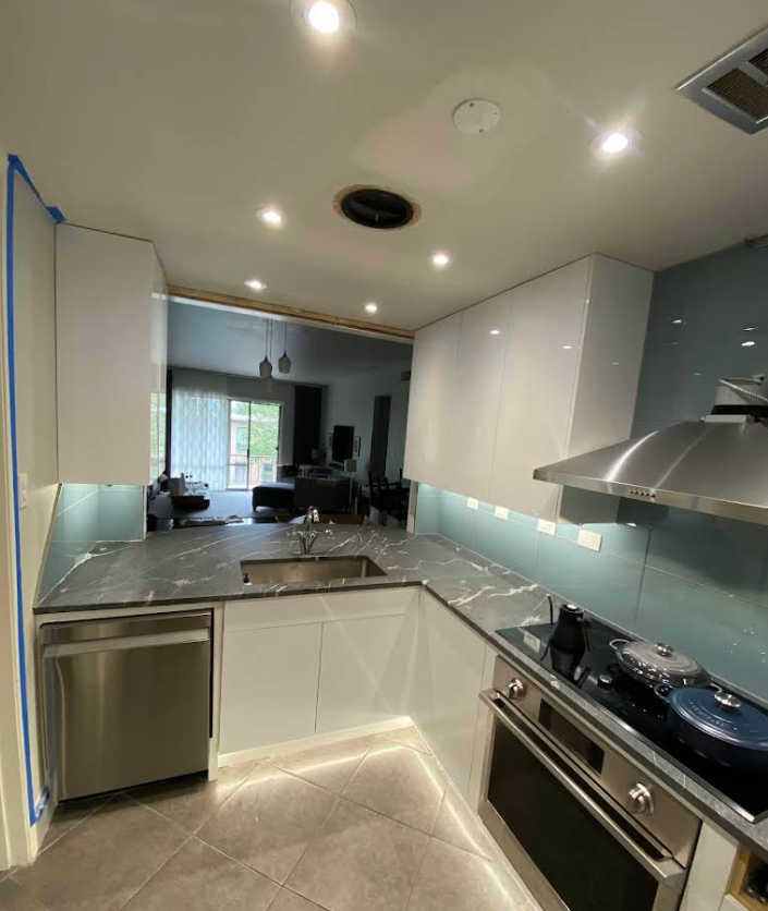 A modern kitchen featuring white cabinets, dark marble countertops, a blue glass backsplash, and stainless appliances.