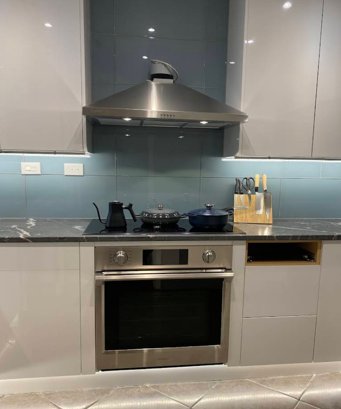 A modern kitchen featuring a stainless steel oven and range hood with a blue glass backsplash and dark marble countertops.