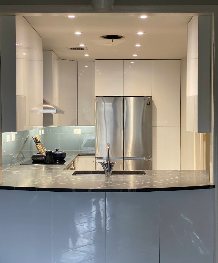 A modern, minimalist kitchen featuring glossy white cabinets, stainless steel appliances, and a gray countertop.