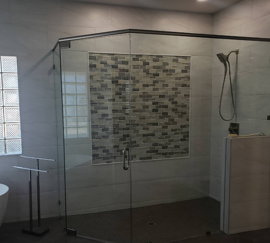 A walk-in shower with a glass enclosure, grey tiled walls, a decorative mosaic tile accent wall, and a handheld showerhead.