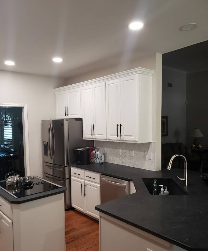 A kitchen with white cabinets, dark countertops, stainless steel appliances, and wood flooring.