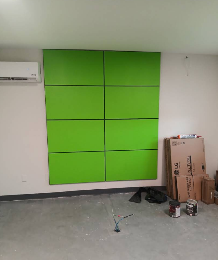 A wall featuring a grid of eight large, bright green rectangular panels, with an air conditioner and boxes nearby.