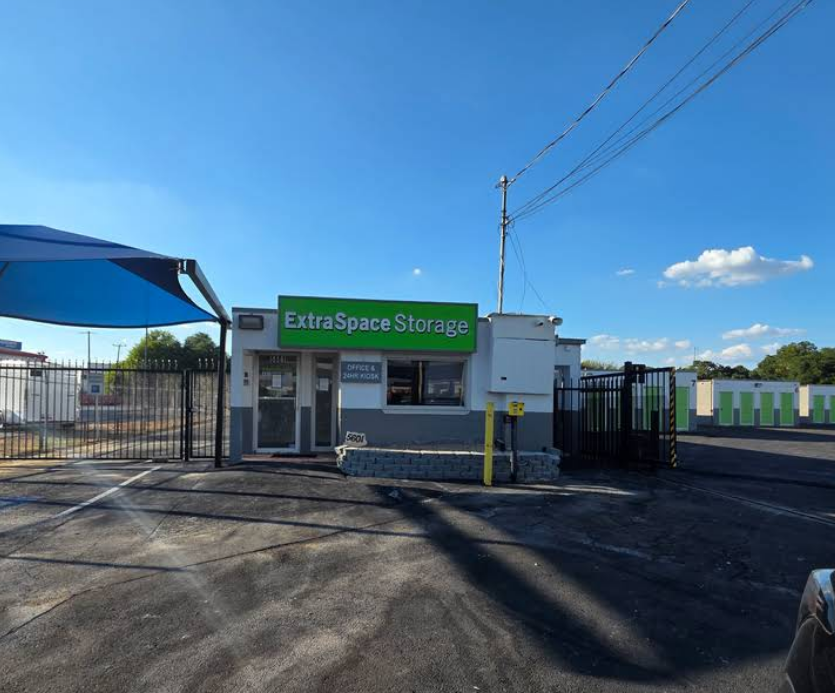 The office building for an Extra Space Storage facility under a clear blue sky, with a fenced parking lot in the foreground.