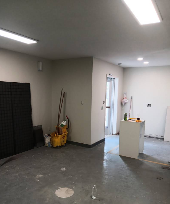 An empty room with gray concrete floors, white walls, a yellow mop bucket, and a doorway leading to another area.