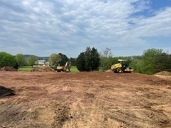Construction site with yellow excavators grading a wide dirt lot under a cloudy sky