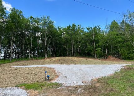 Gravel clearing beside a wooded area with a blue utility pipe and a tree line under a clear sky