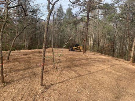 Cleared dirt lot in wooded area with a yellow bulldozer near trees