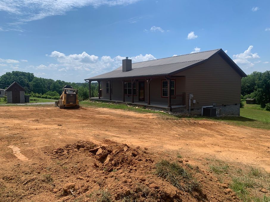 New house under construction on a dirt lot with a backhoe and clear blue sky