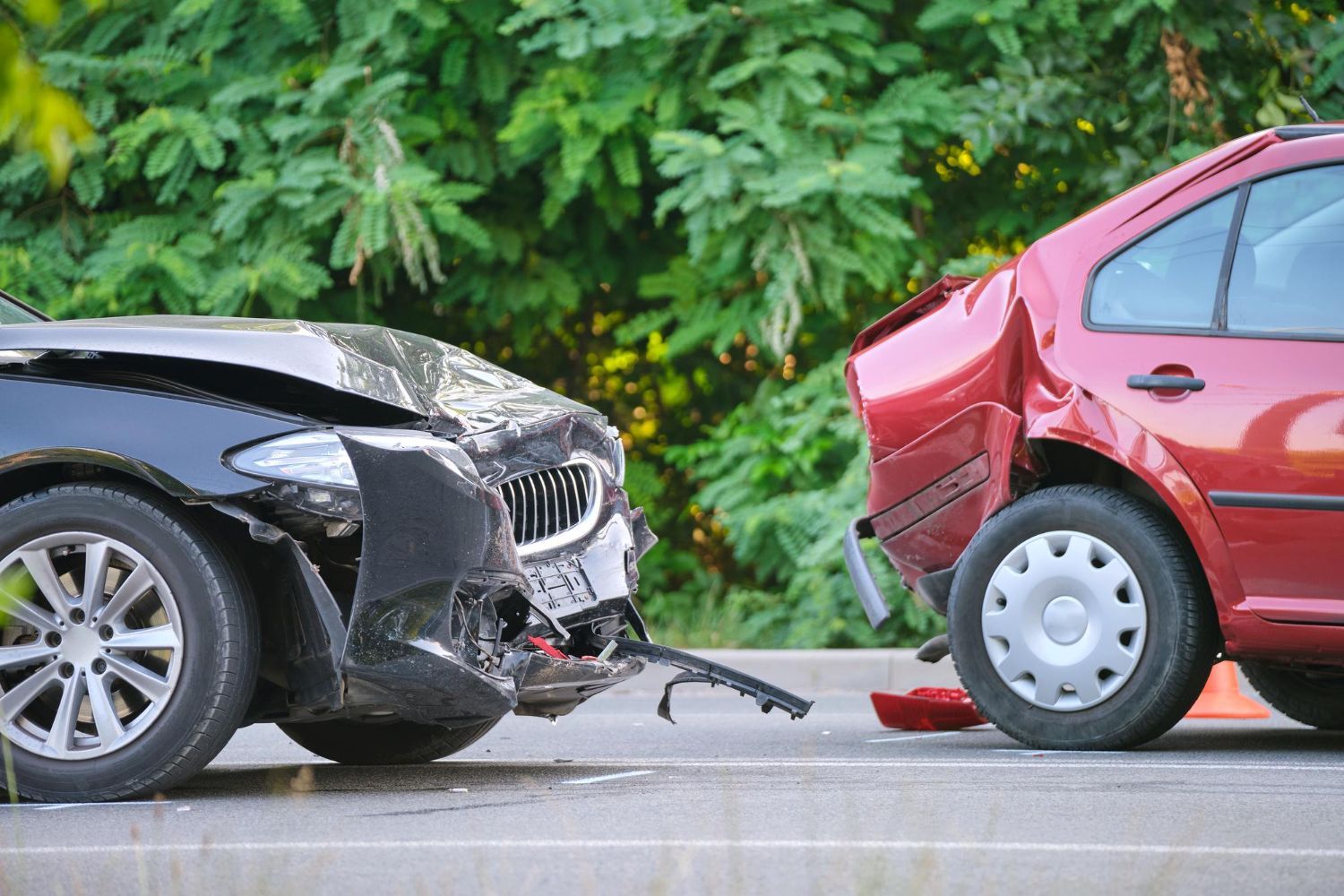 Two cars with severe front-end damage after a collision on a road, black car hitting red car