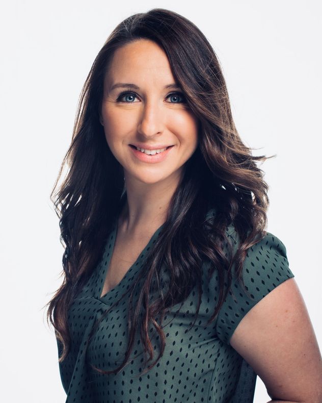 Portrait of a smiling woman with long dark hair, wearing a green patterned top on a light background