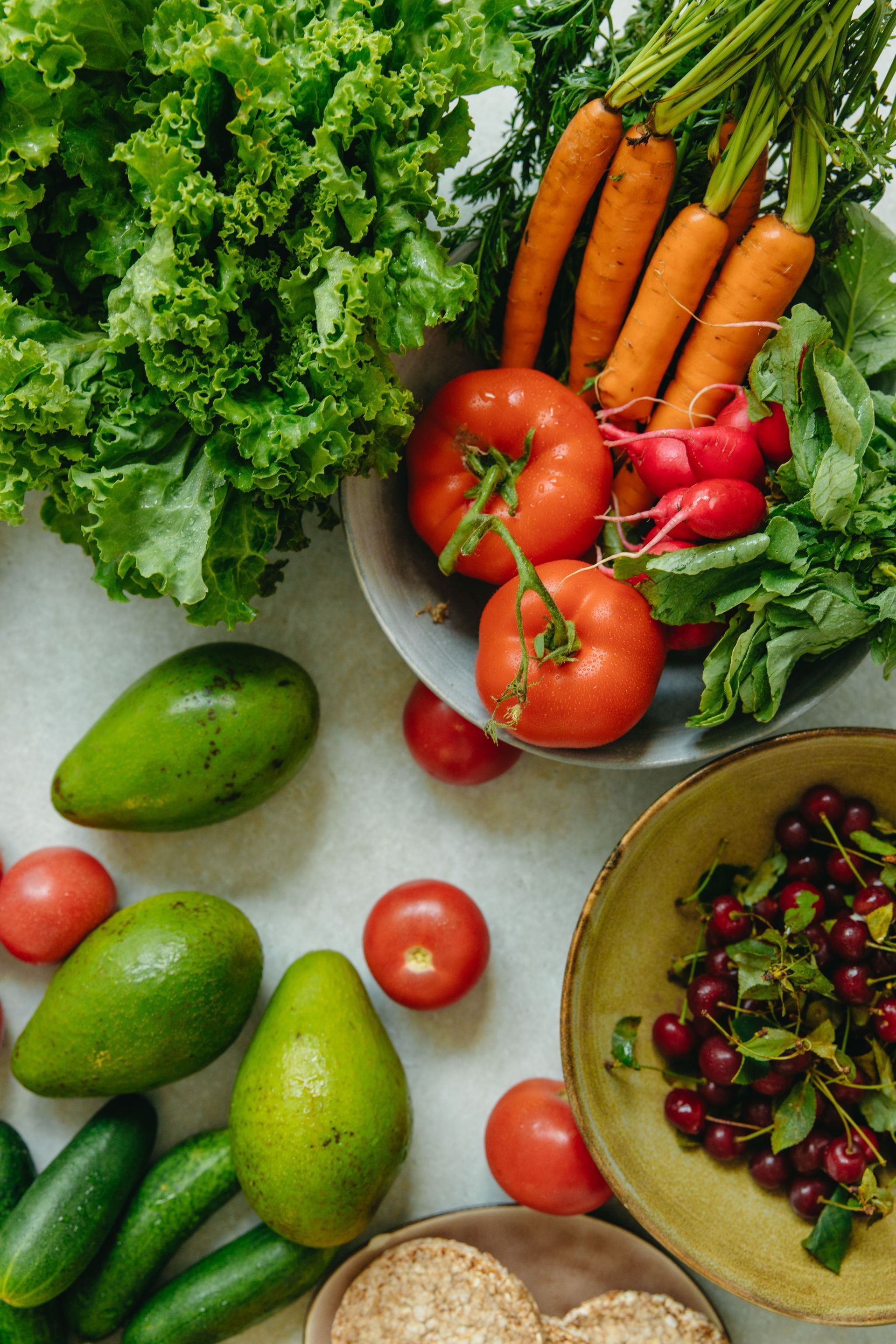 Variedad de frutas y verduras frescas sobre una mesa, incluyendo lechuga, zanahorias, tomates, aguacates y cerezas.