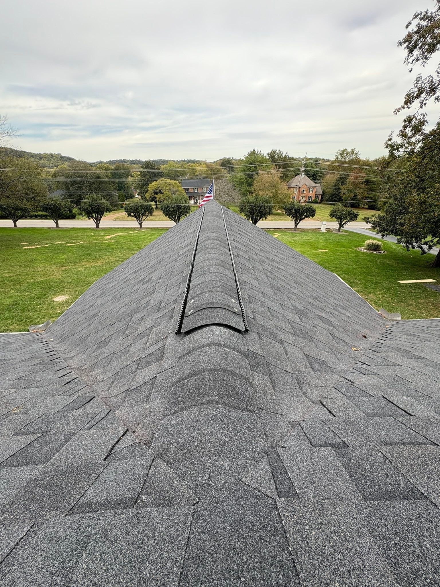 Gravel rooftop ridge leading to a tree-lined landscape under a cloudy sky
