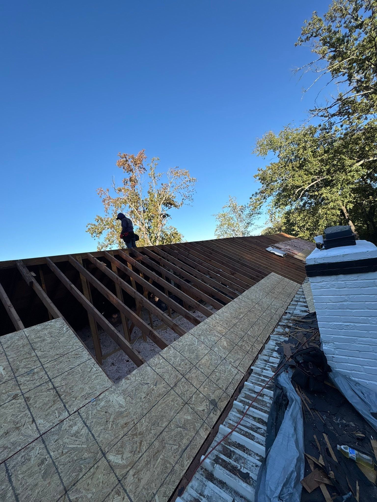 Worker on a steep roof installing dark shingles under a clear blue sky
