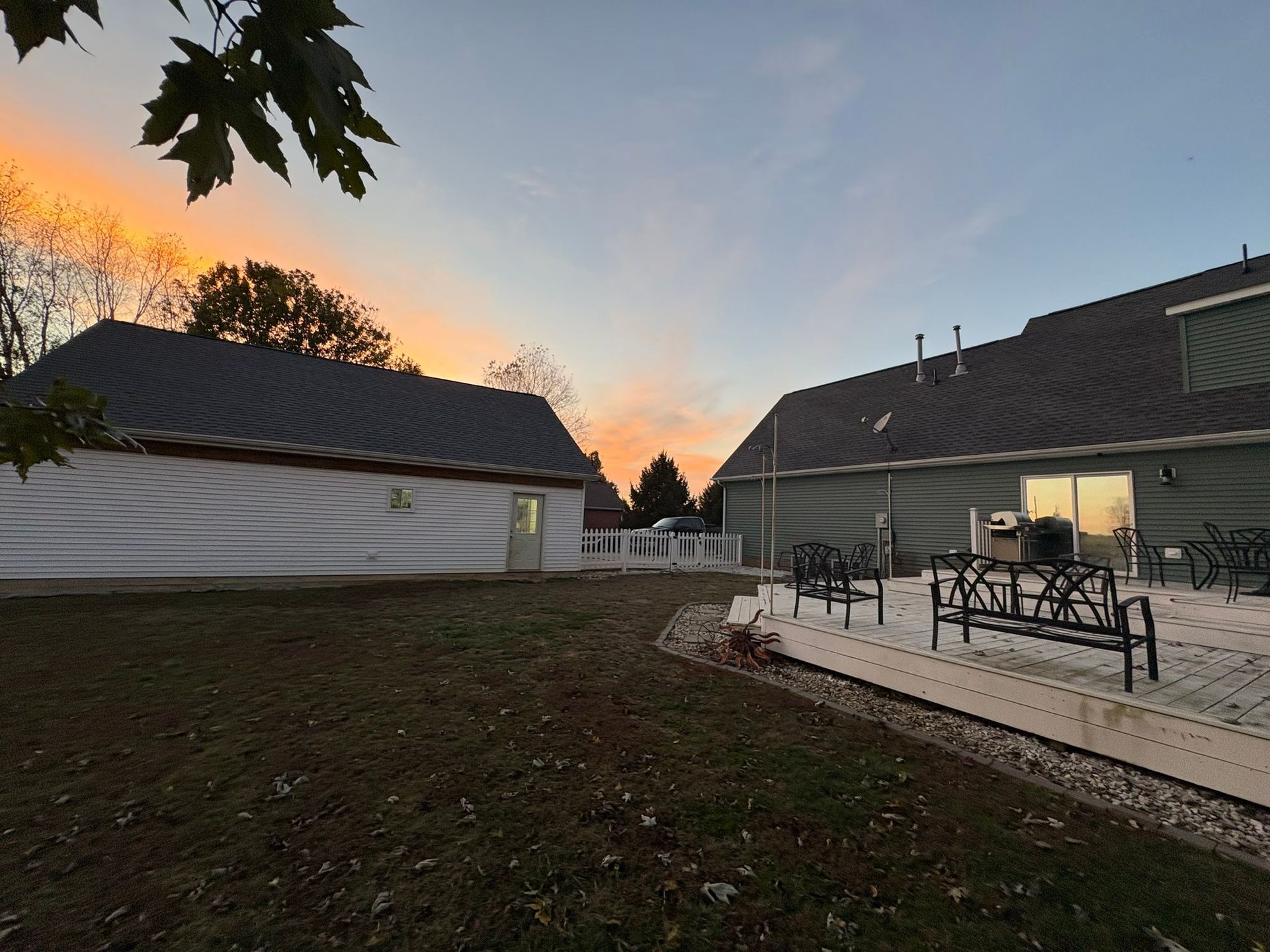 Sunset over a backyard patio with outdoor chairs and a lit house beside a white tent-like structure