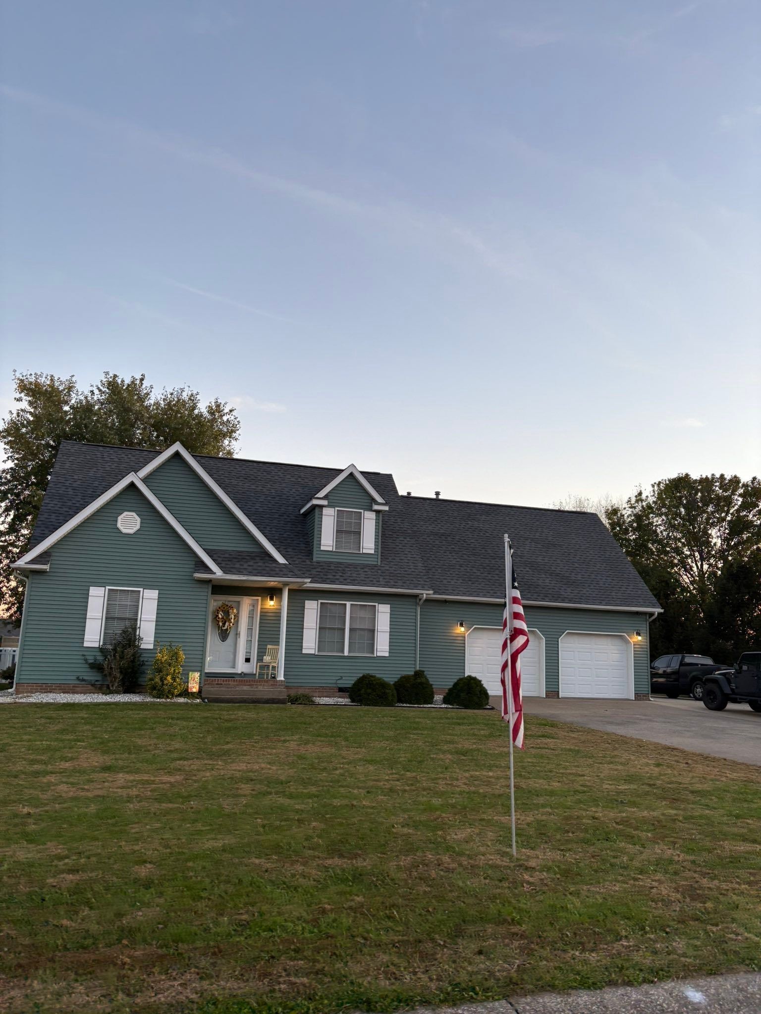Suburban house with green siding, a two-car garage, and a U.S. flag in the front yard at dusk