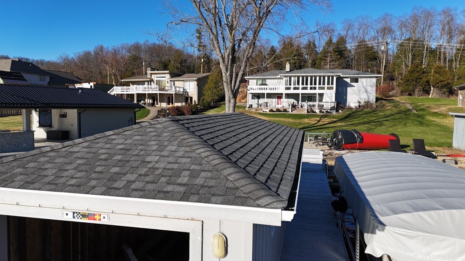 Roofing materials on a residential rooftop, with houses and trees in the background under a clear blue sky