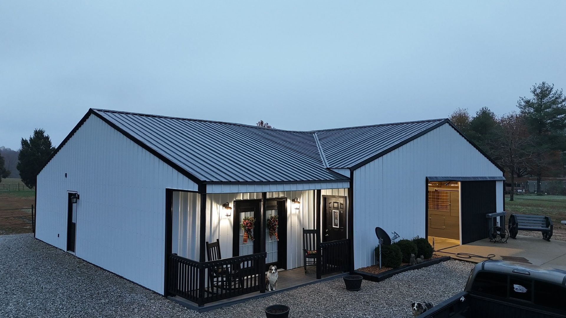 White modern house with lit windows at dusk and a gravel yard