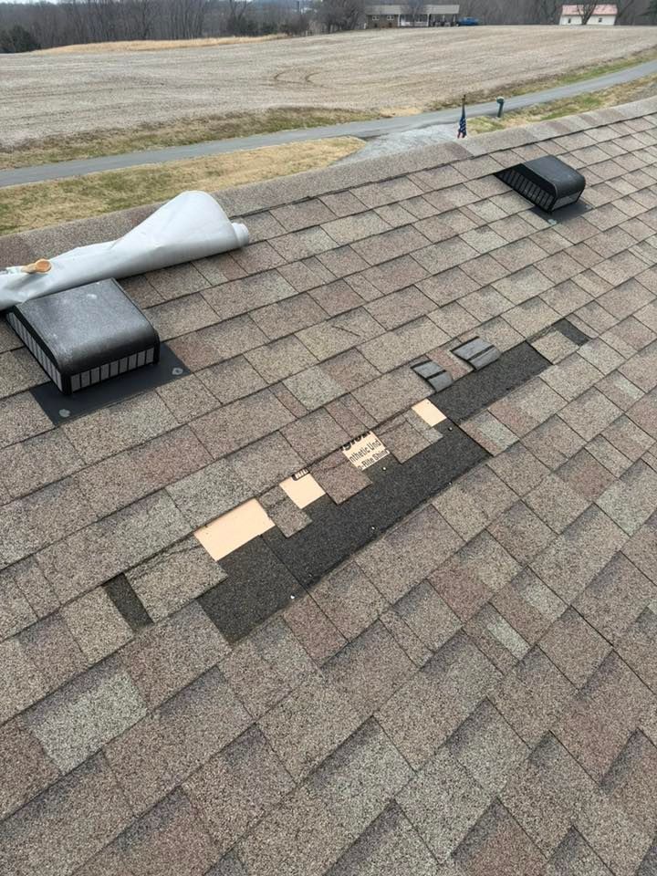 Rooftop with damaged shingles, two vent pipes, and a torn white membrane near the ridge.
