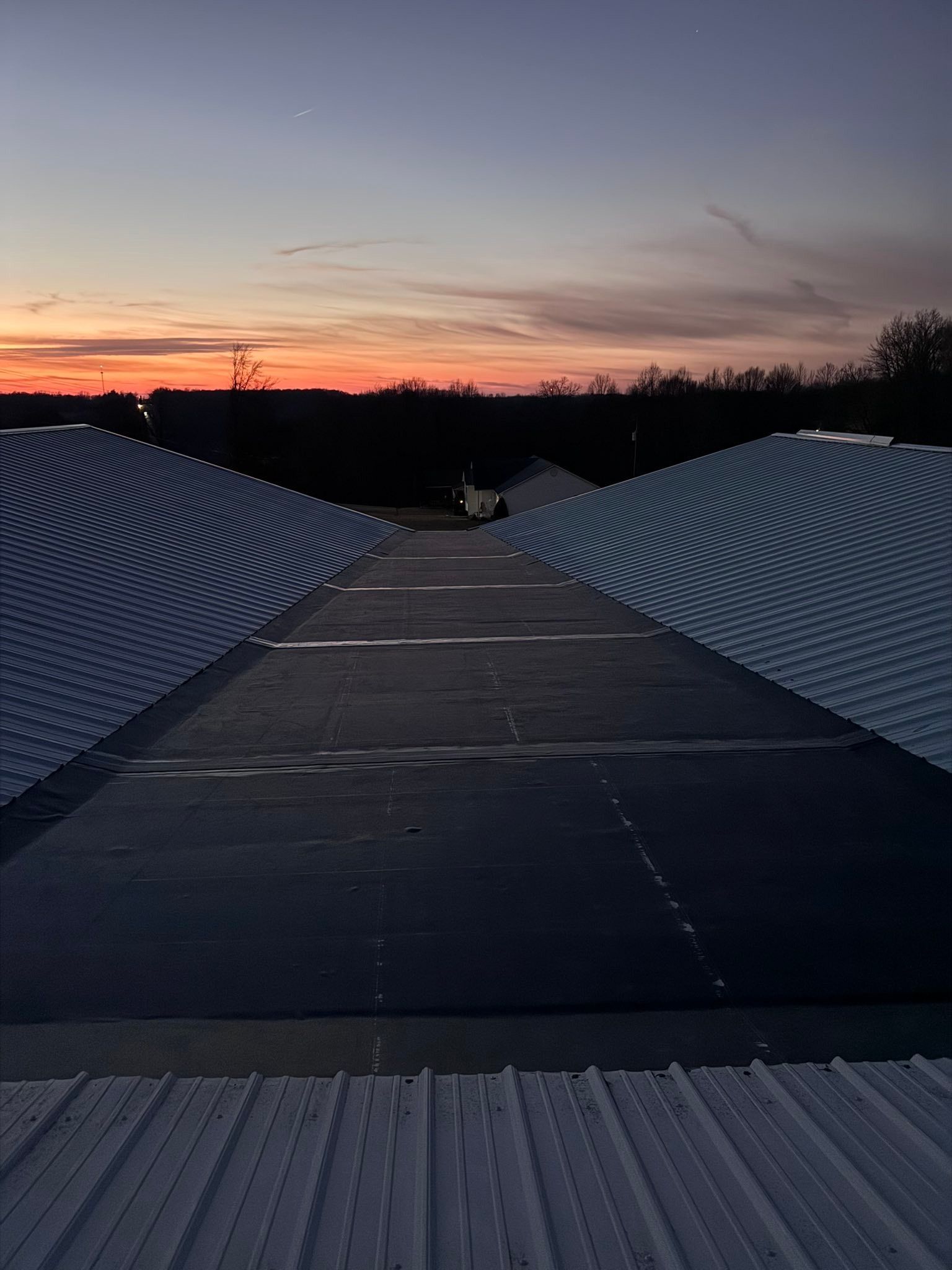 A wooden walkway between patterned metal walls at sunset, with a pink-orange sky