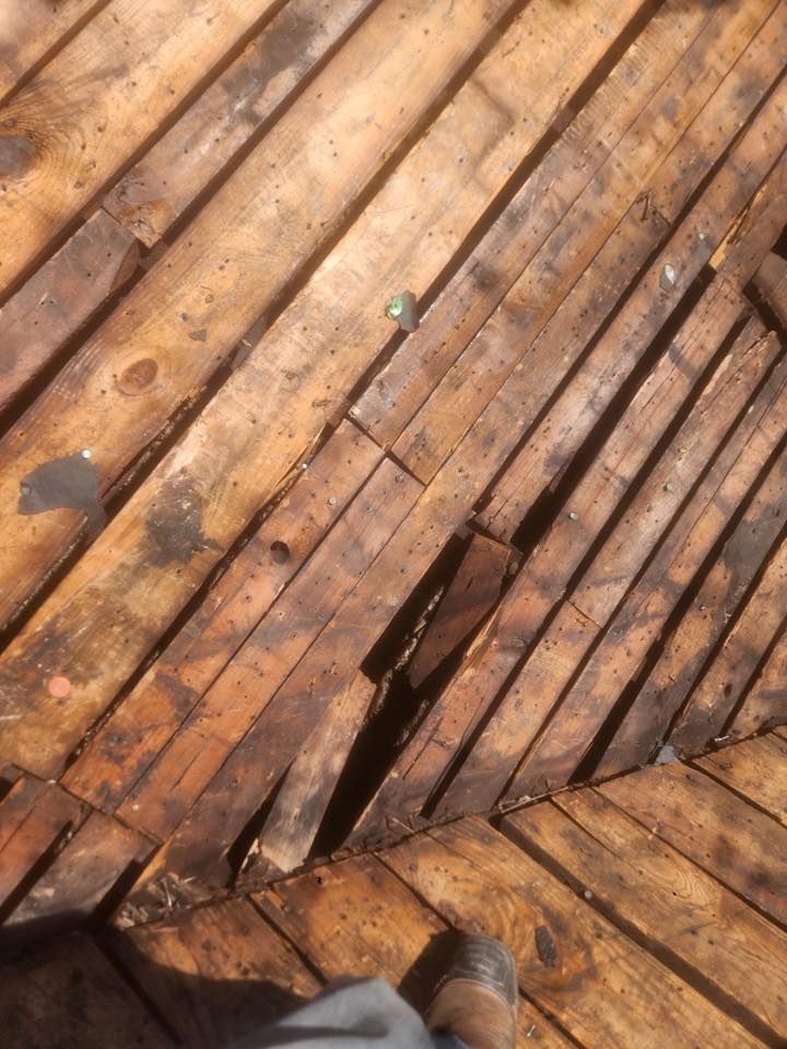Close-up of a wooden deck with a large crack and missing plank, showing a shoe at the bottom edge