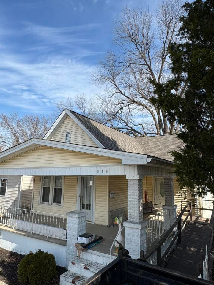 Small yellow house with a front porch, white trim, and bare trees under a blue sky
