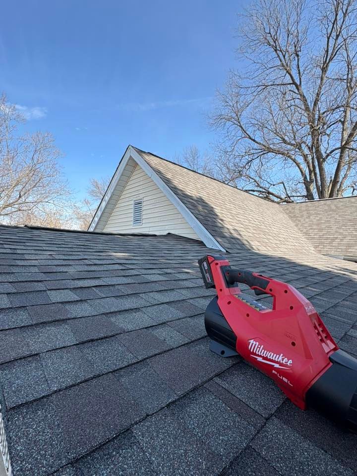 Red Milwaukee tool on a shingled roof beside a house under a blue sky
