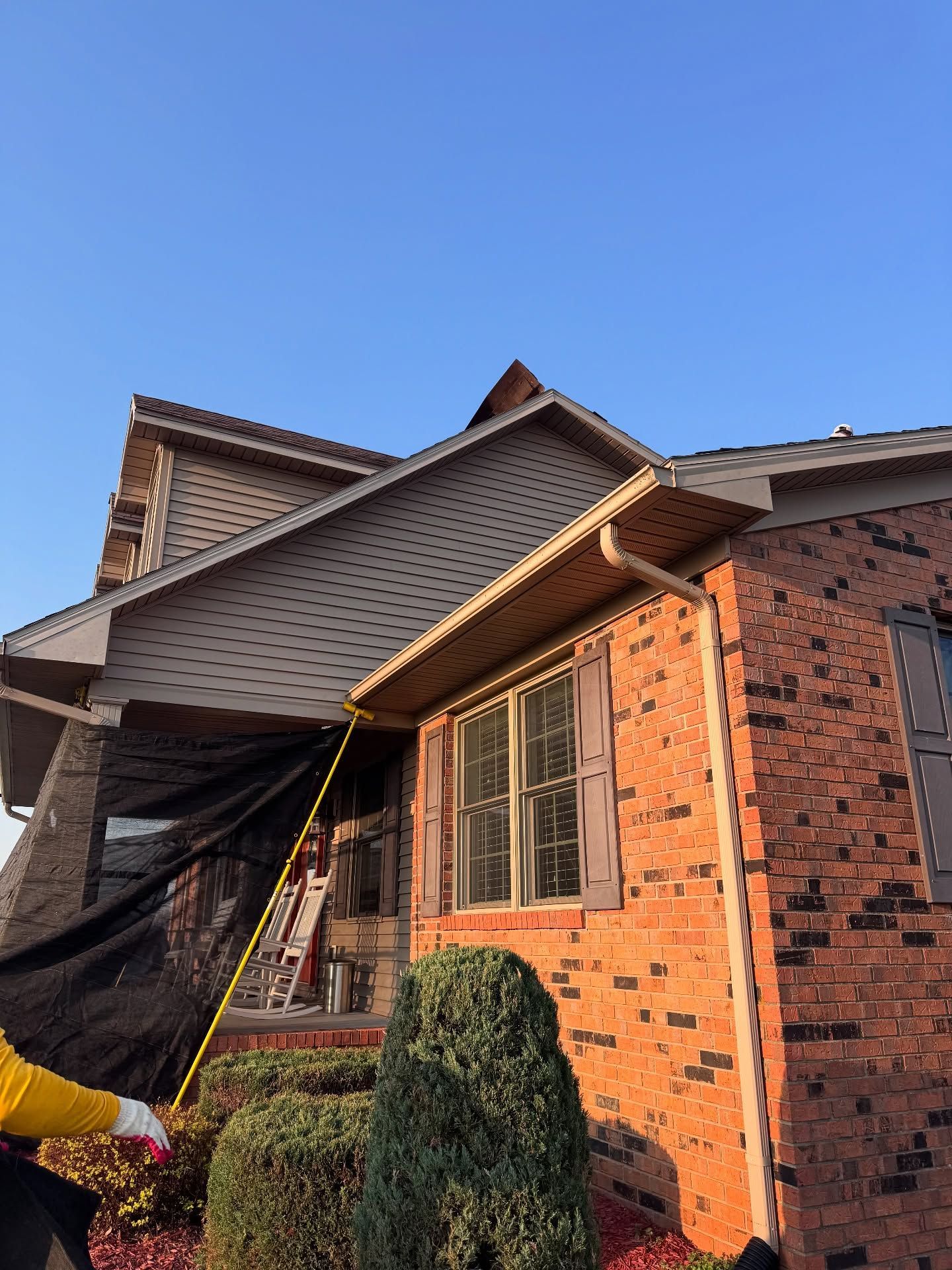 Brick house exterior with a sloped roof, windows, and a small tree under a clear blue sky