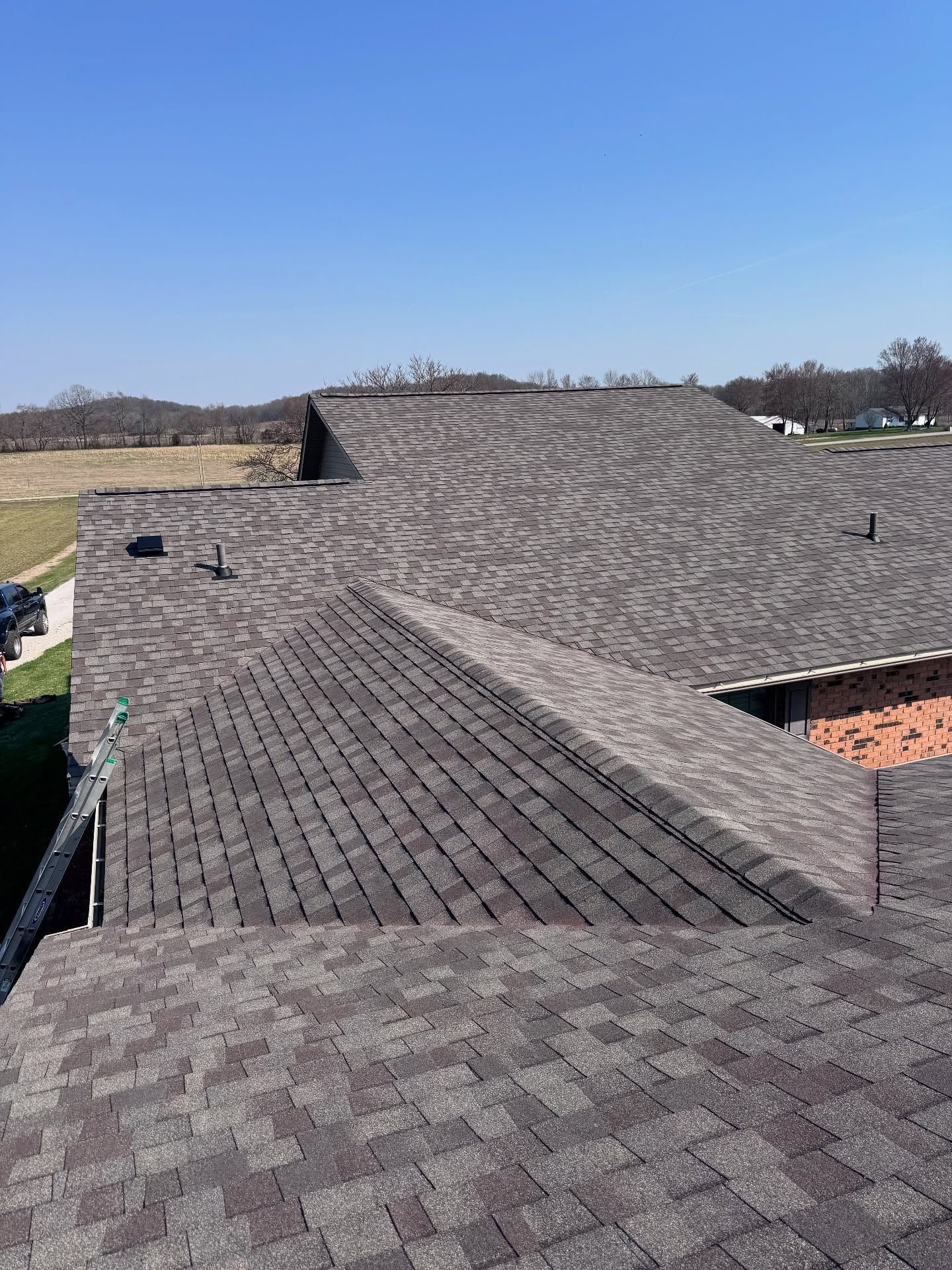 Rooftop under construction with gray shingles and a clear blue sky in the background