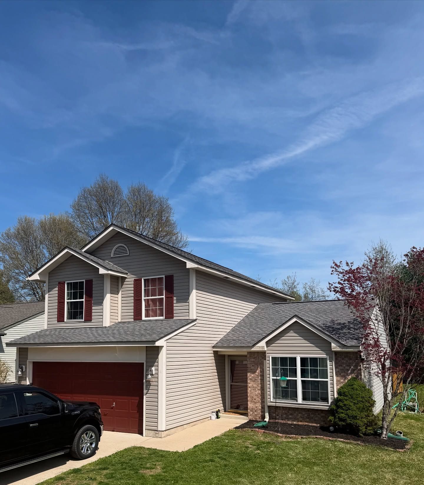 Suburban two-story house with gray siding, red garage door and shutters, under a clear blue sky