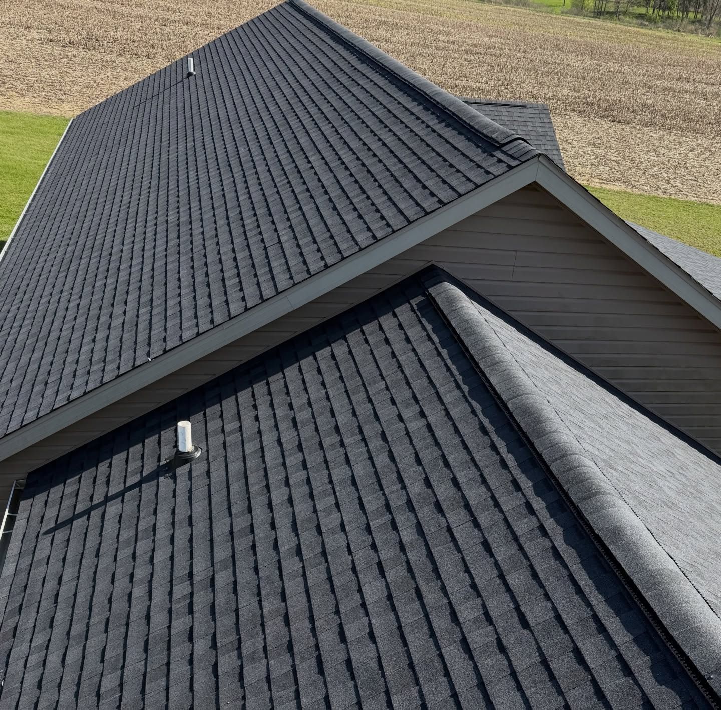 Aerial view of a dark gray shingled roof with a small skylight and adjoining roof sections.