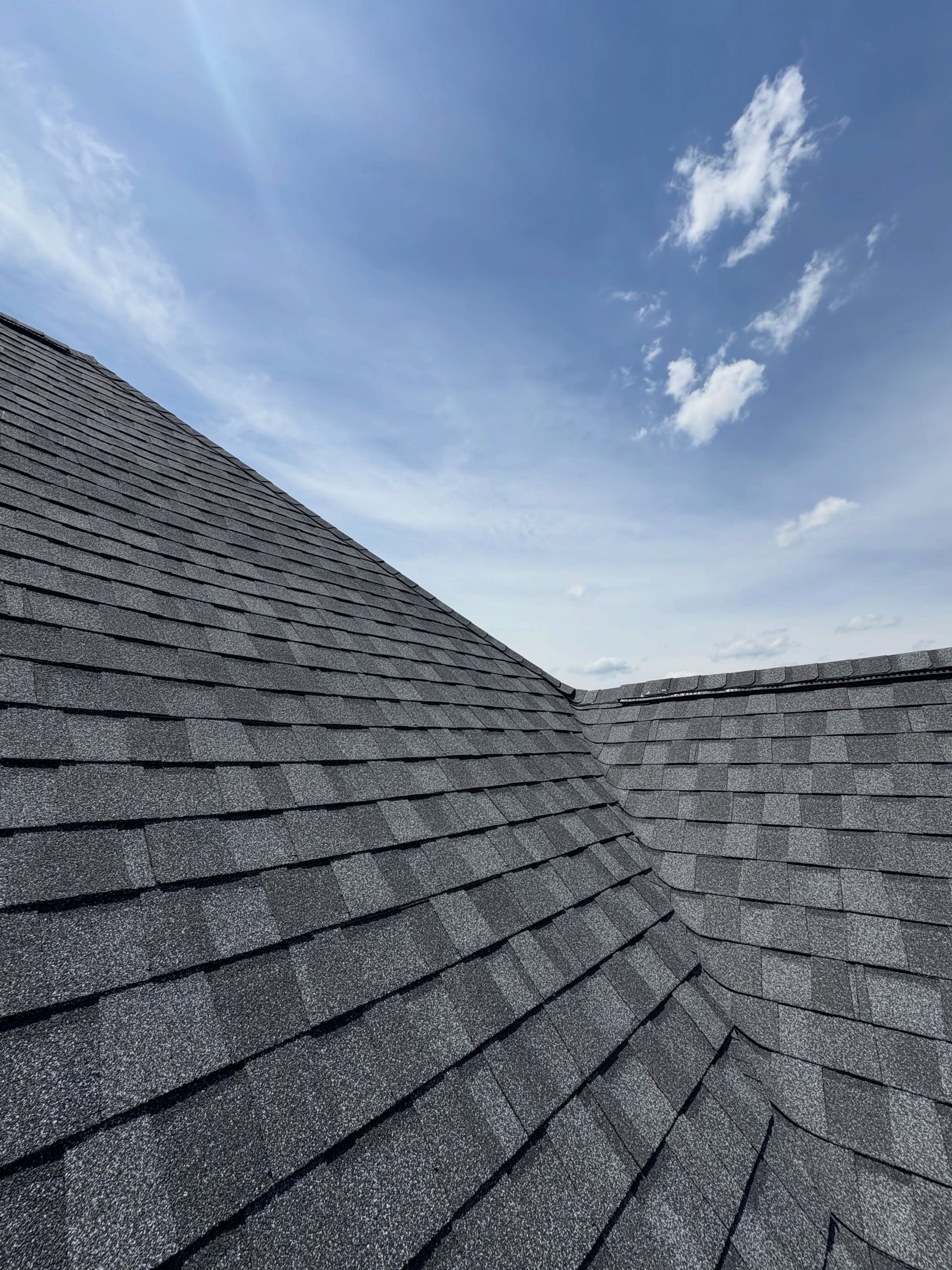 Gray shingle roof under a bright blue sky with wispy clouds