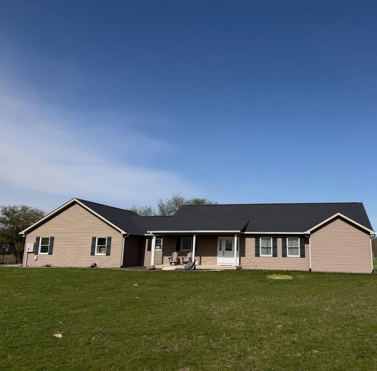 Single-story beige house with dark roof on a grassy hill under a clear blue sky