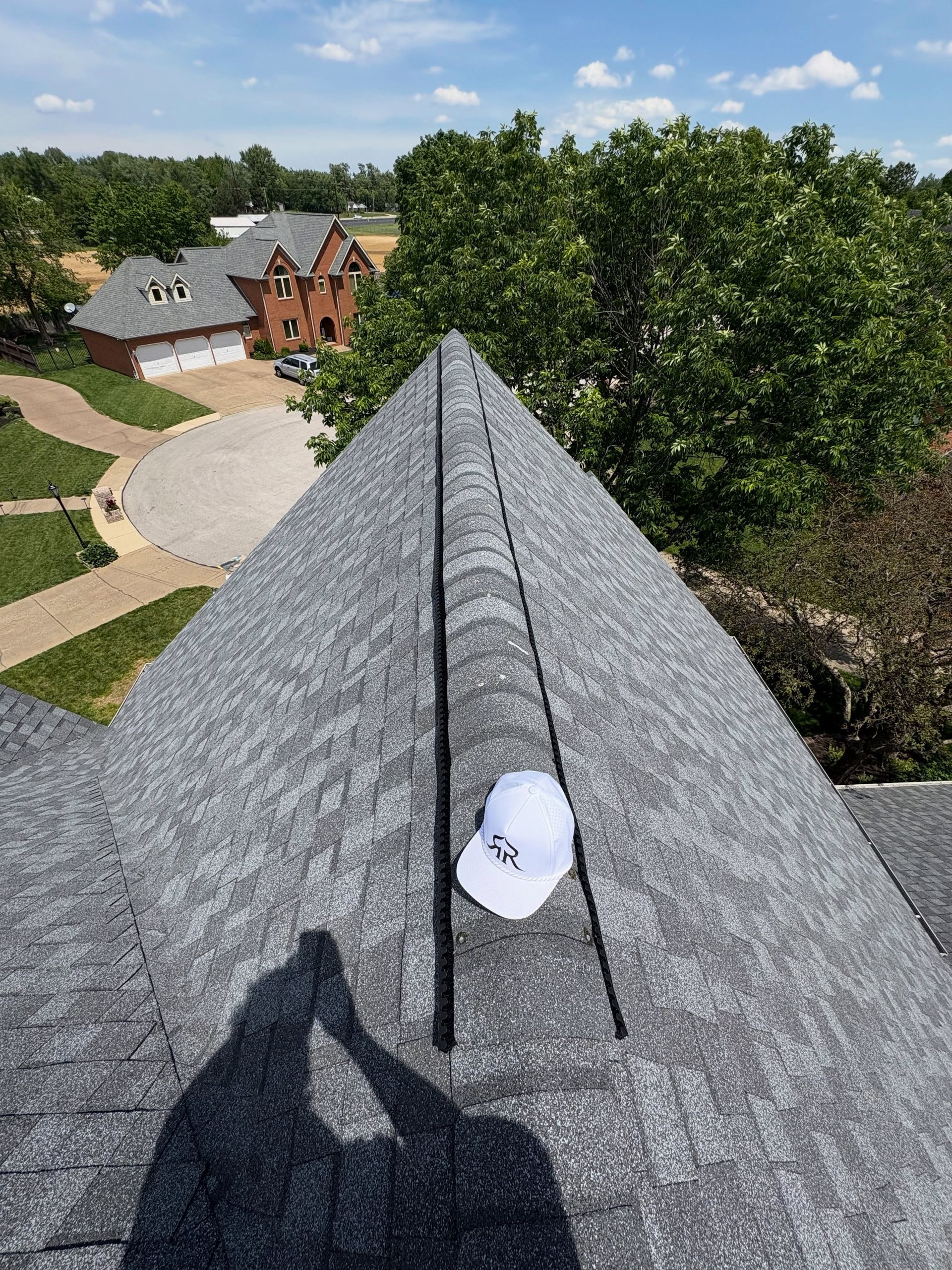 View from a shingled rooftop toward houses, trees, and a white cap near the peak