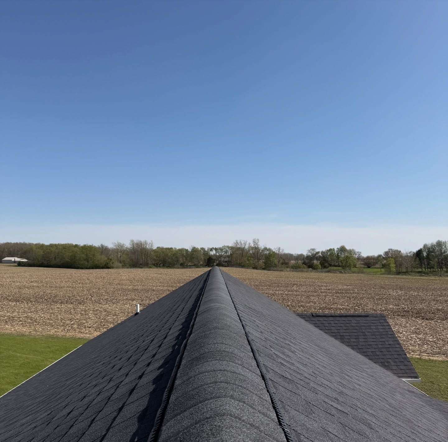 Rooftop ridge view over fields and trees under a clear blue sky