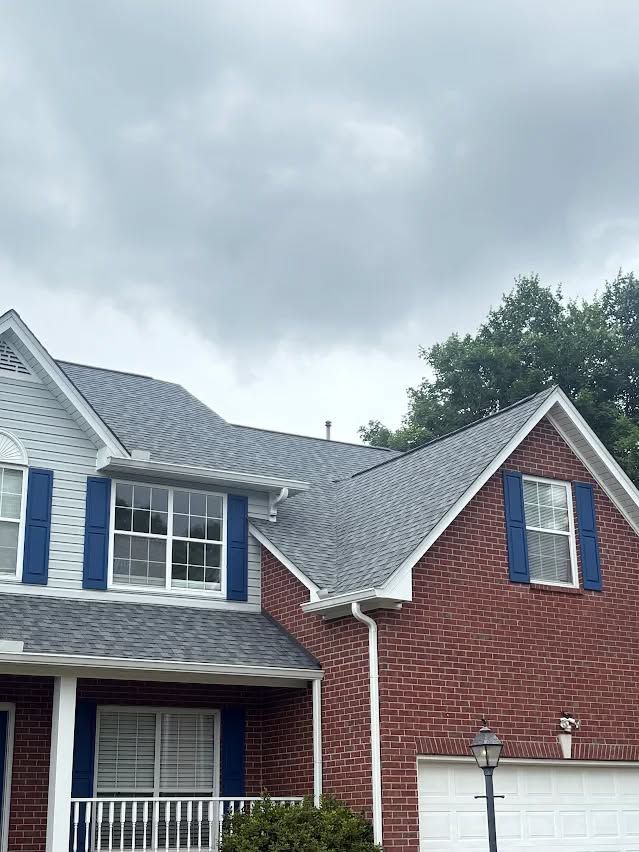 Two-story brick and siding house with blue shutters under a cloudy sky