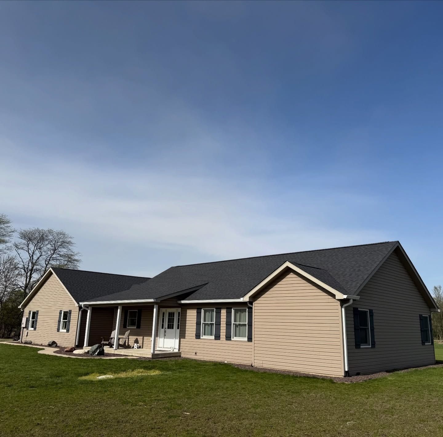 Single-story beige ranch house with dark roof and covered front porch on a grassy lot