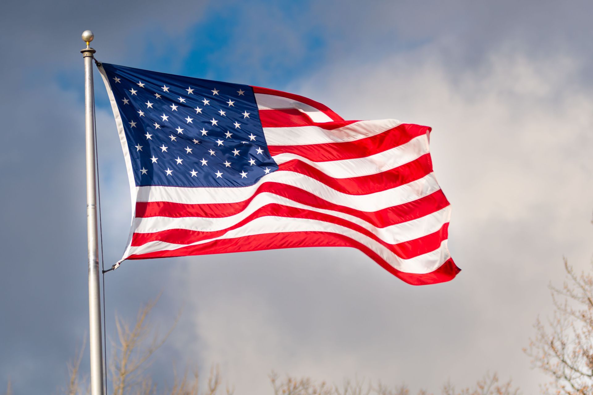 American flag waving on a flagpole against a cloudy sky