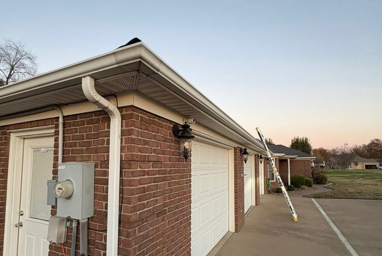 Brick building corner with white doors, downspout, and a long ladder leaning against the wall at dusk