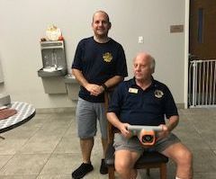 Two men, one standing and one seated, with a medical device in a room.