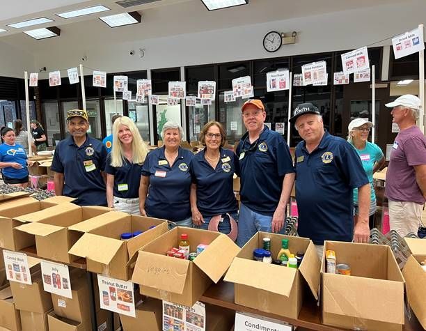 Volunteers at a food drive sort donations. People in blue shirts stand behind boxes of food.