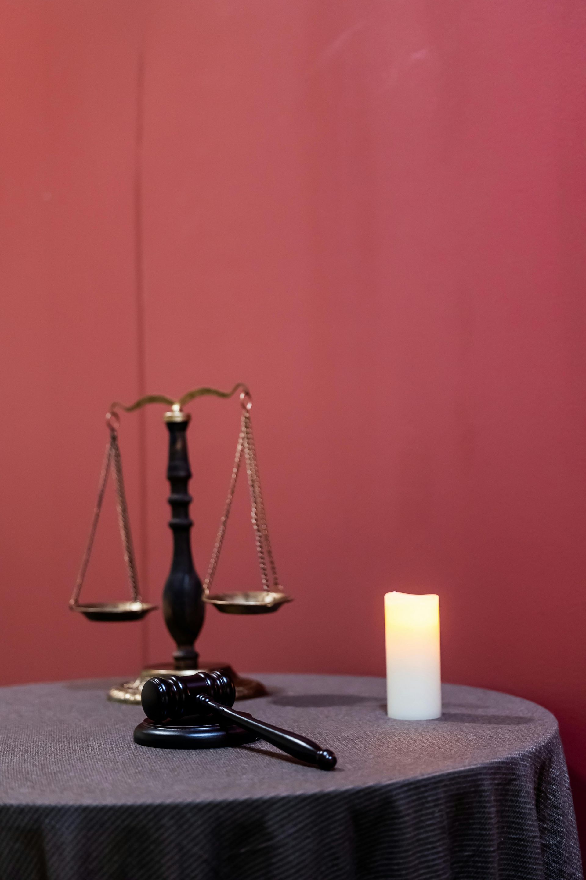 Judge's scales and a gavel beside a lit candle on a table against a red background